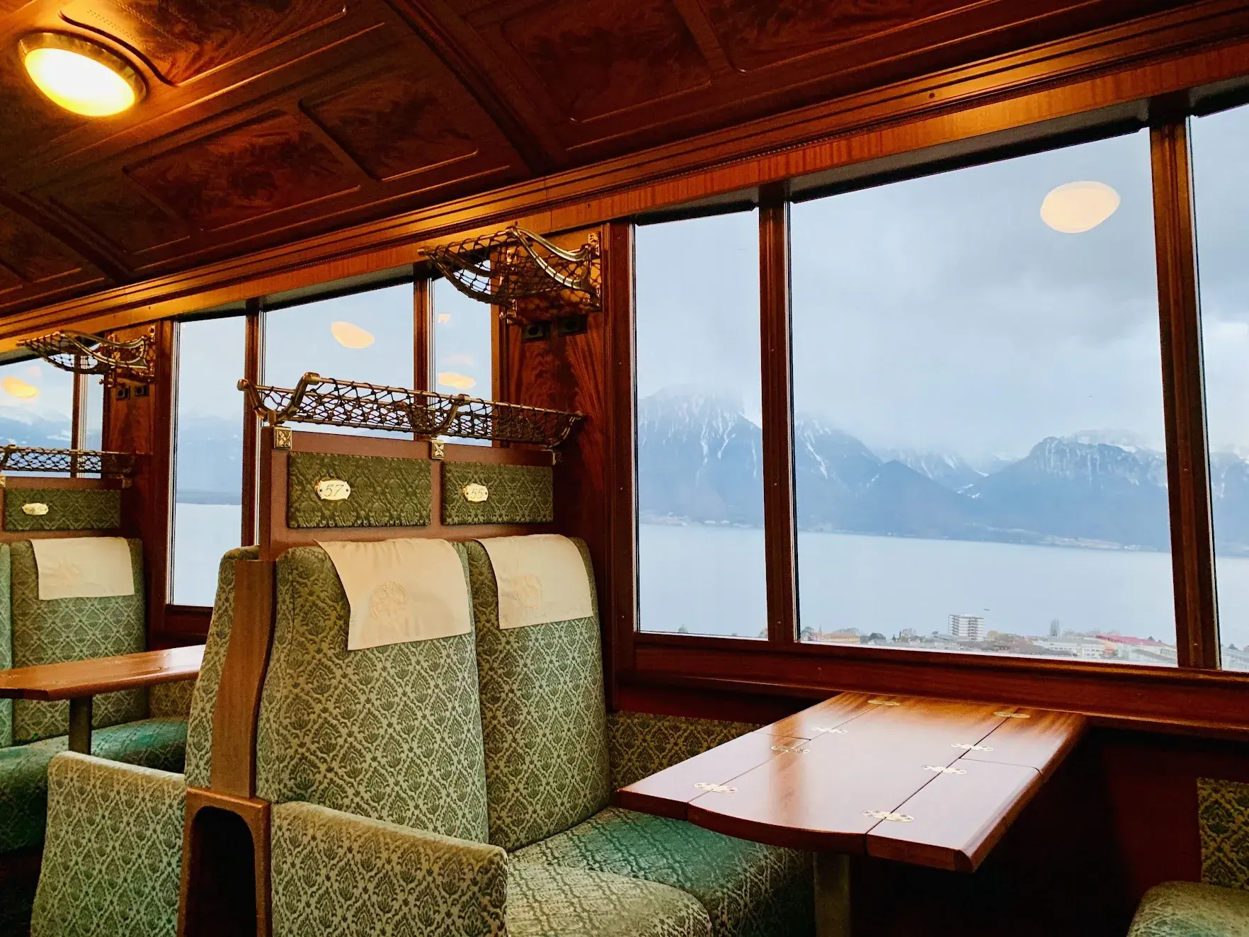 Inside a Belle Époque carriage of the MOB railway: wood panelling, green upholstered seats and a view of Lake Geneva