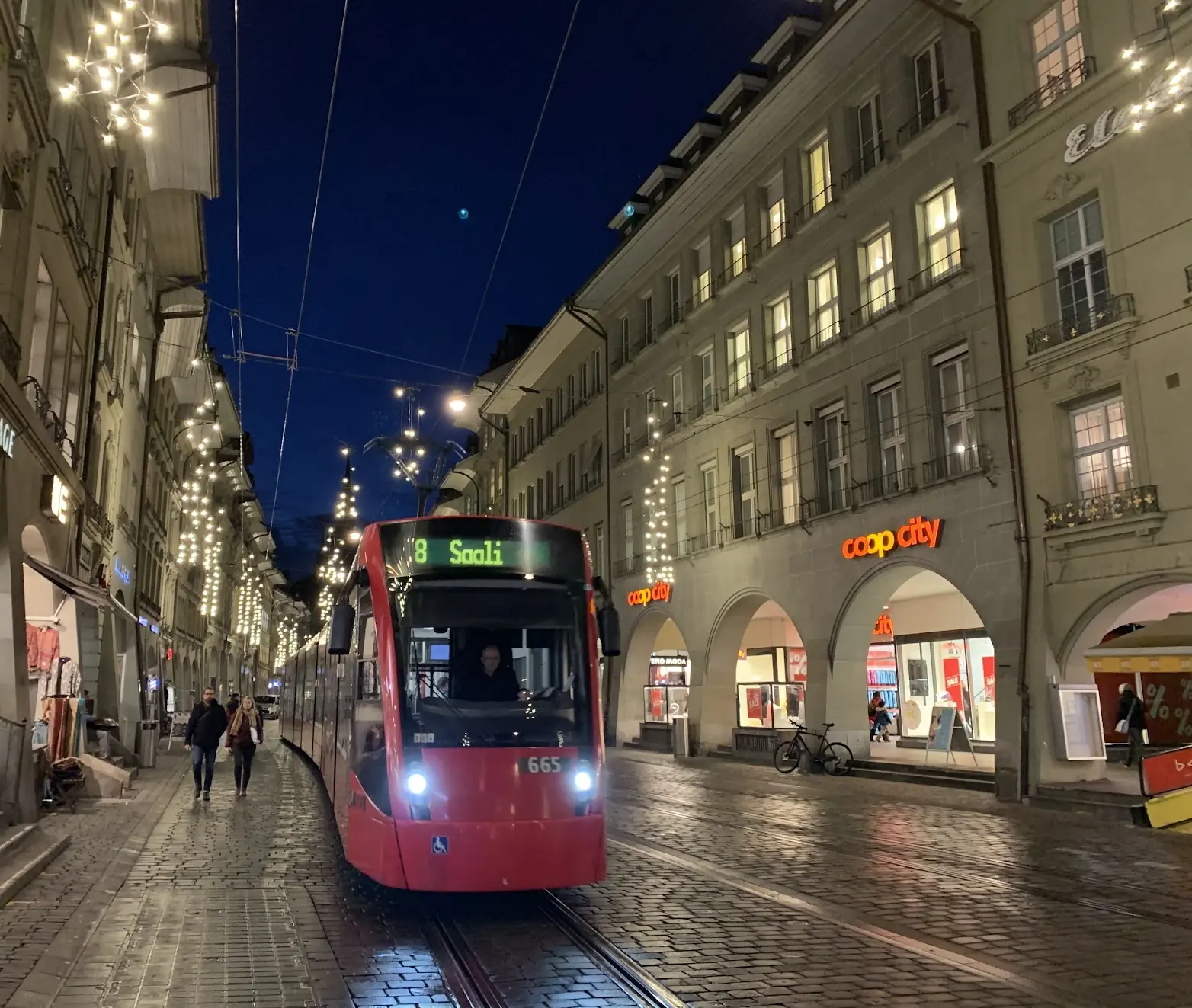 A red Bern tram on a cobbled street with Christmas lights at dusk