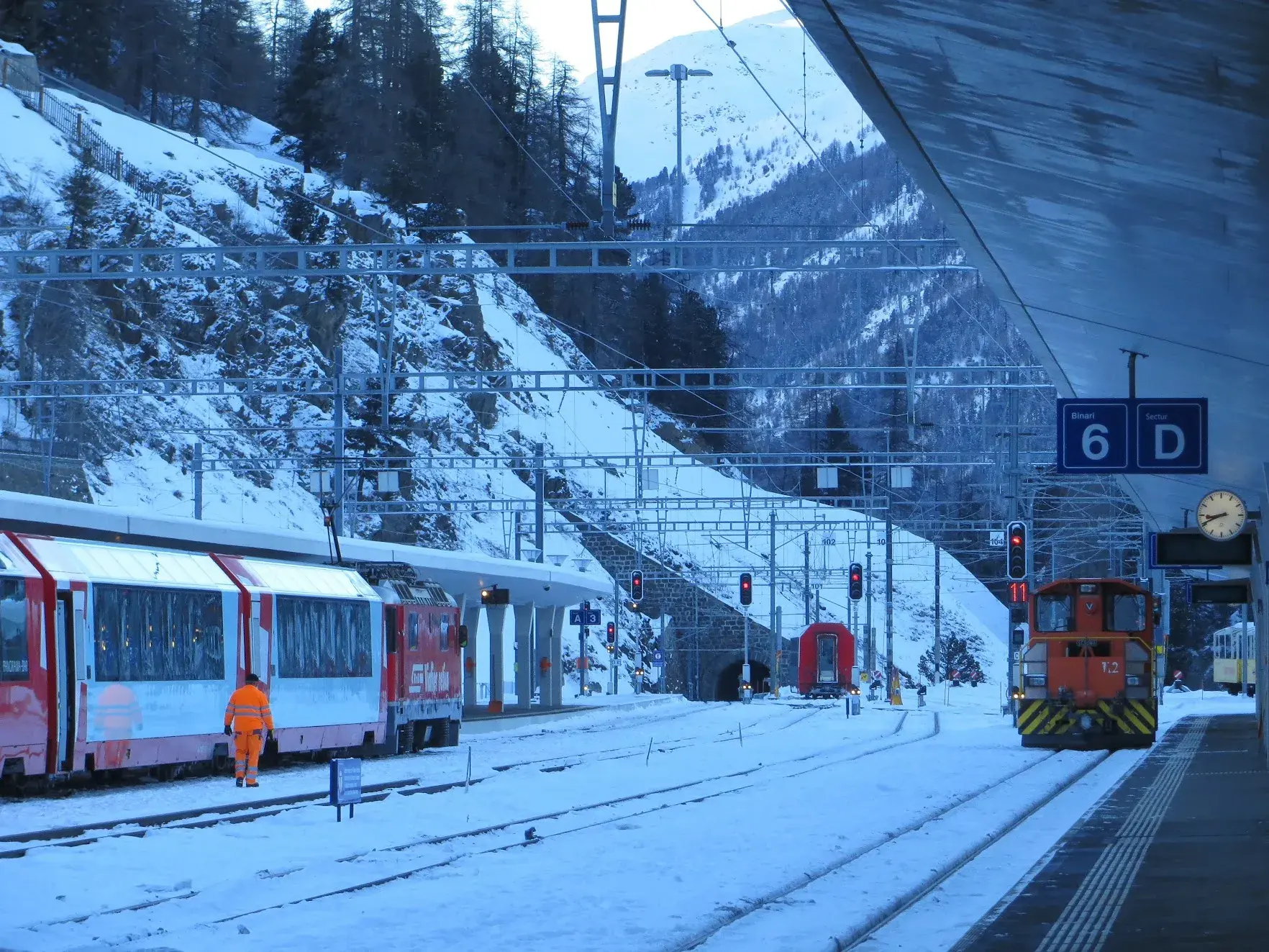 Glacier Express panoramic carriages at St. Moritz station in the snow, with a railway worker beside the train
