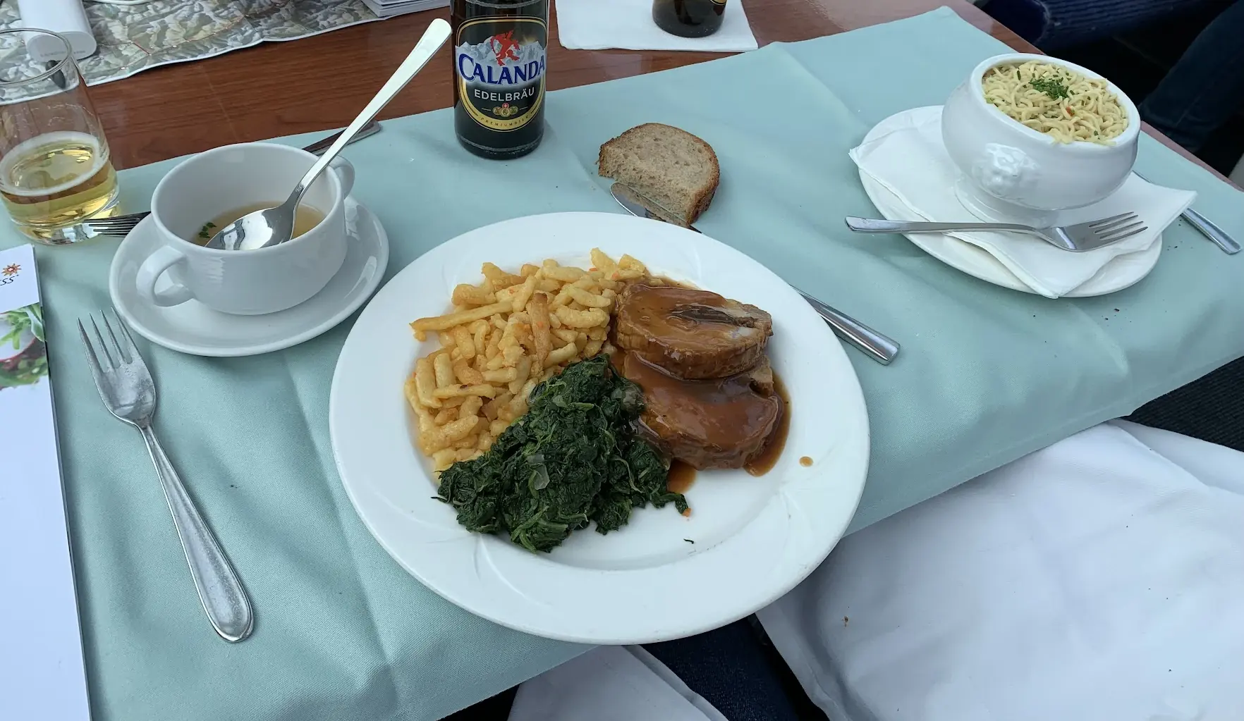 Roast pork with spätzli and spinach, a cup of broth and a Calanda beer on a table on the train
