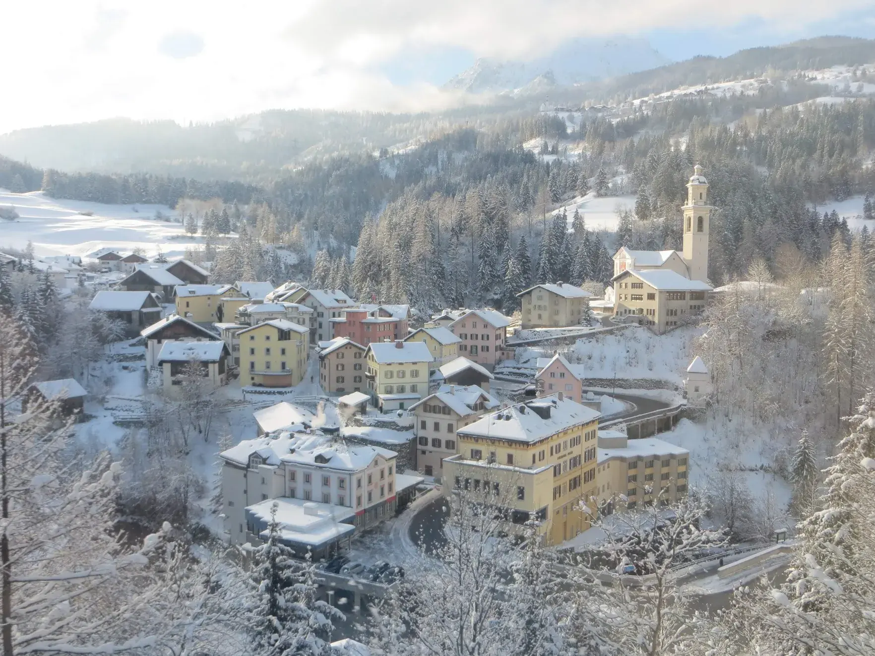 A snow-covered village with pastel houses and a church bell tower, seen from the train