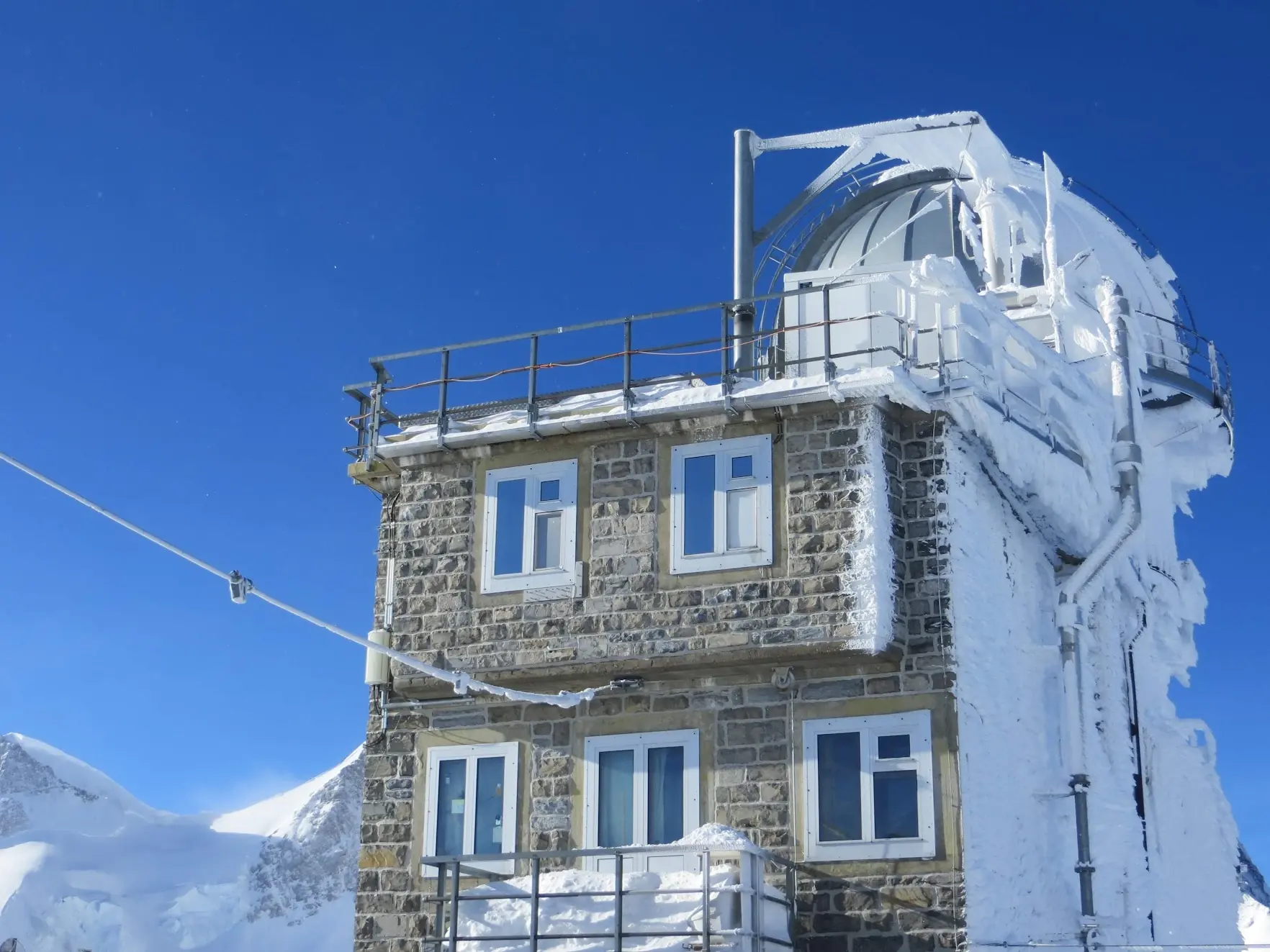 The Sphinx observatory at the Jungfraujoch, a stone building with a dome coated in ice, under a deep blue sky