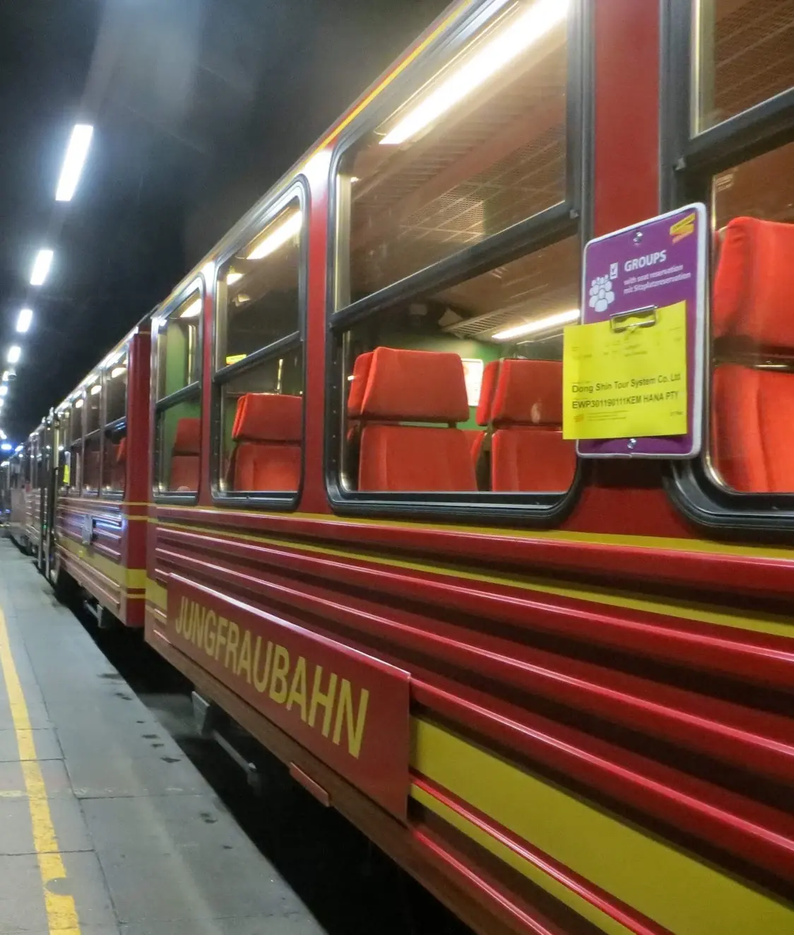 The red Jungfraubahn train with orange seats waiting in the lit tunnel station inside the mountain
