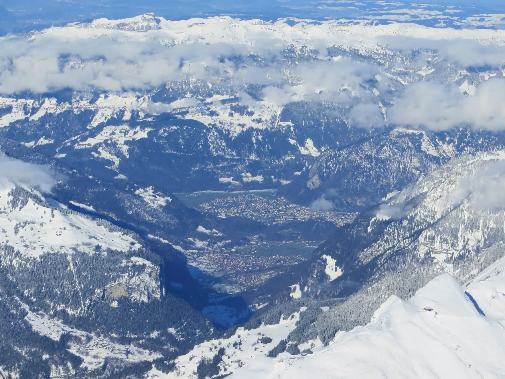 A wide valley with a town far below, seen from high on the Jungfrau, with snowy forests and clouds