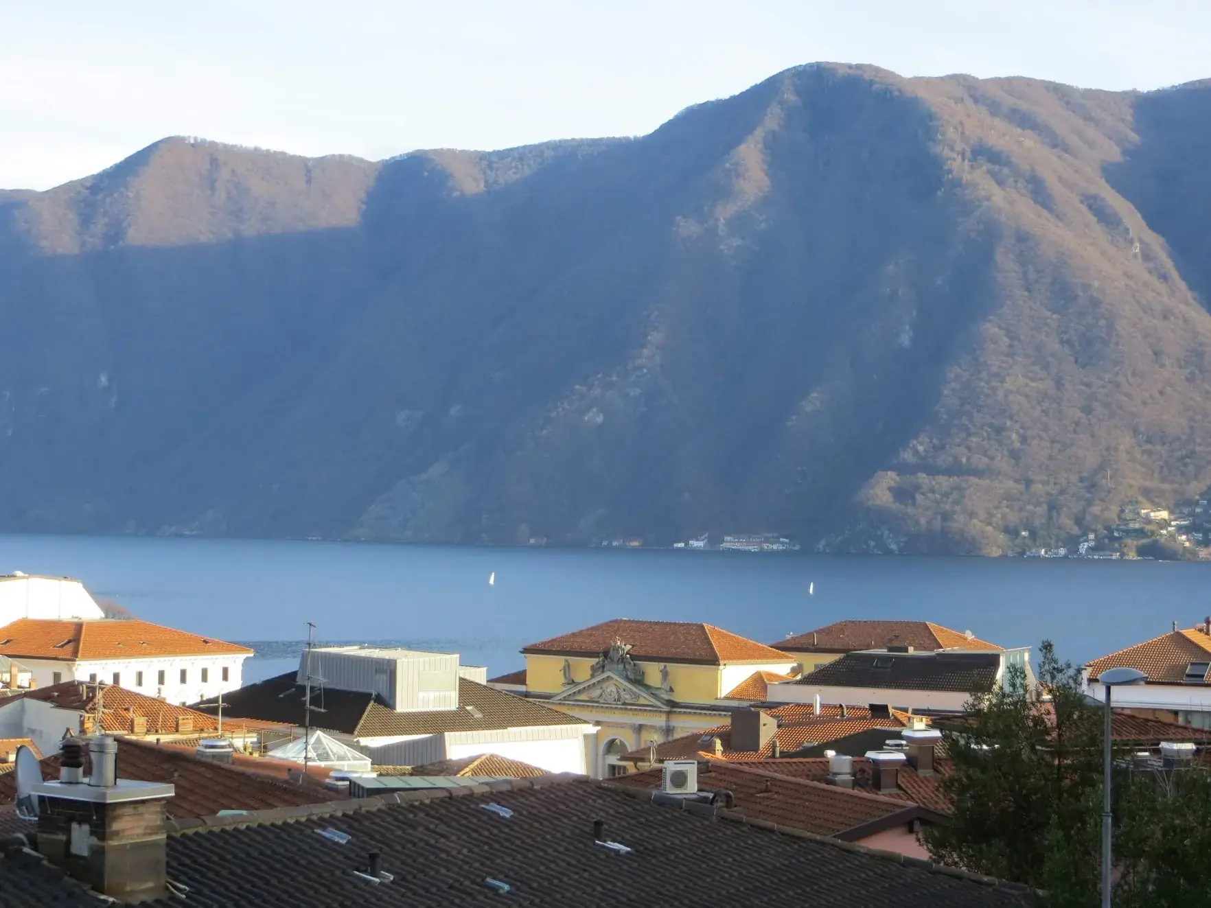 Terracotta roofs of Lugano above the lake, with a steep wooded mountain on the far shore