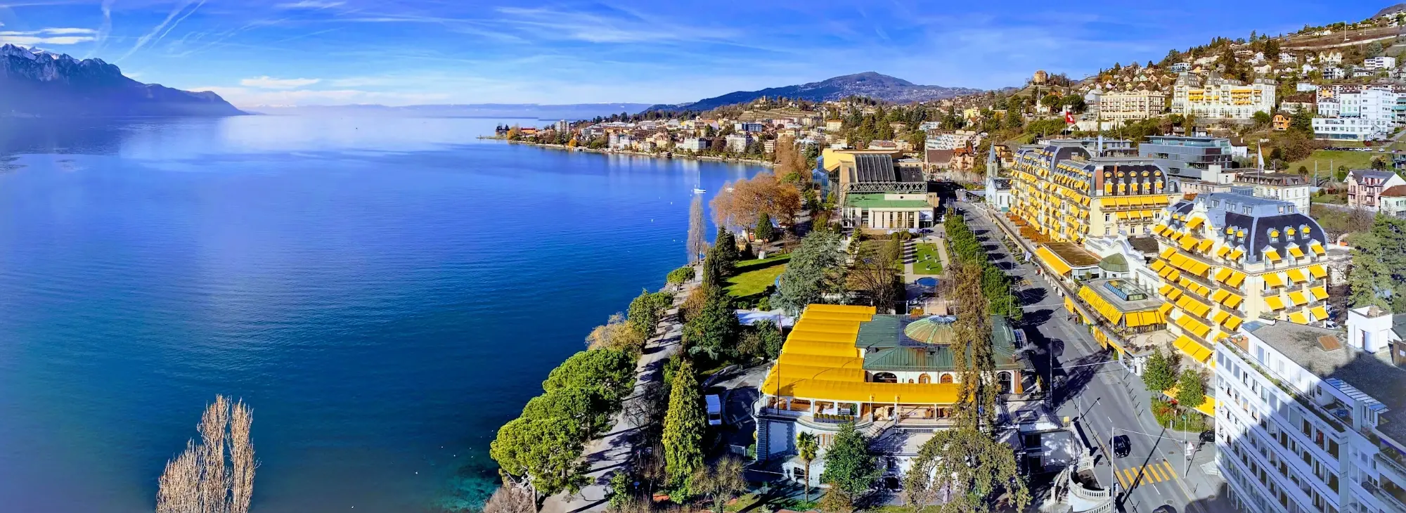 Panorama of Montreux on Lake Geneva, with grand hotels with yellow awnings along the shore and mountains on the far side