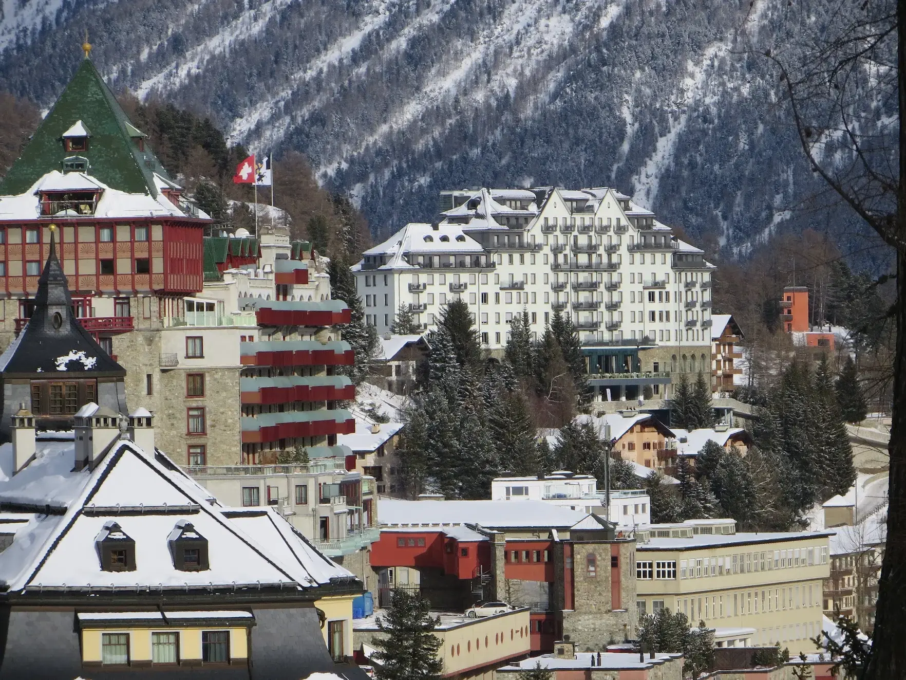 Grand hotels of St. Moritz with snow on the roofs and a forested mountain behind