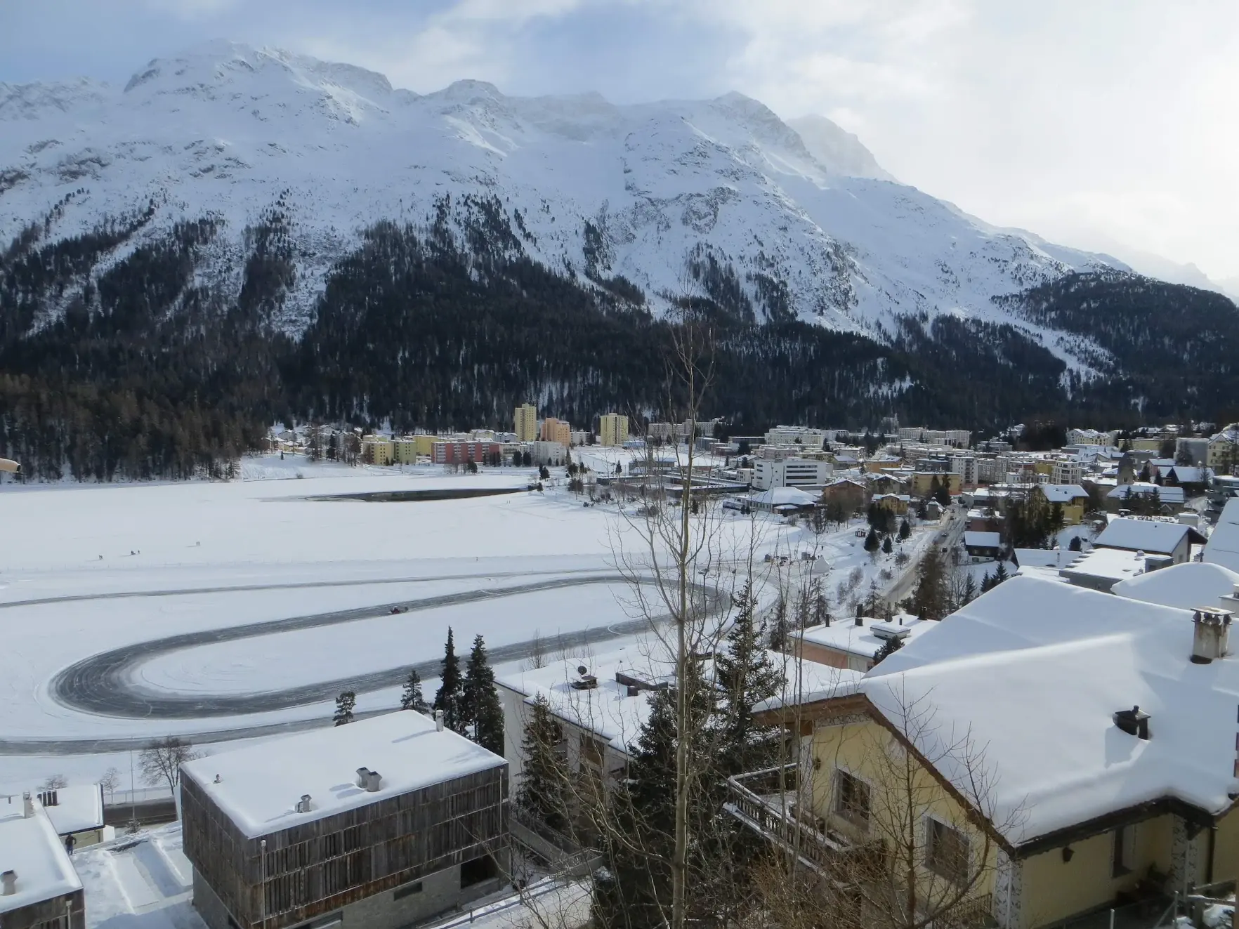The frozen lake of St. Moritz with an ice track, below snowy mountains and the town