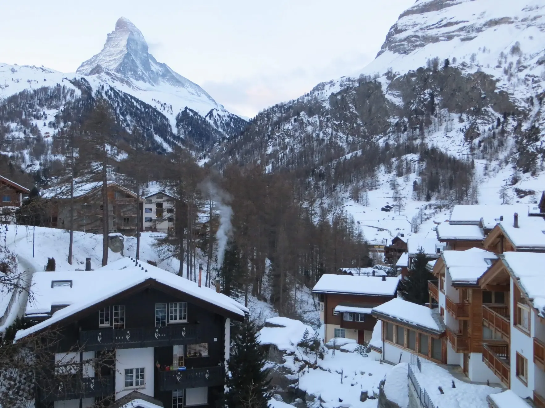 The Matterhorn rising above snowy chalets in Zermatt, with smoke from a chimney