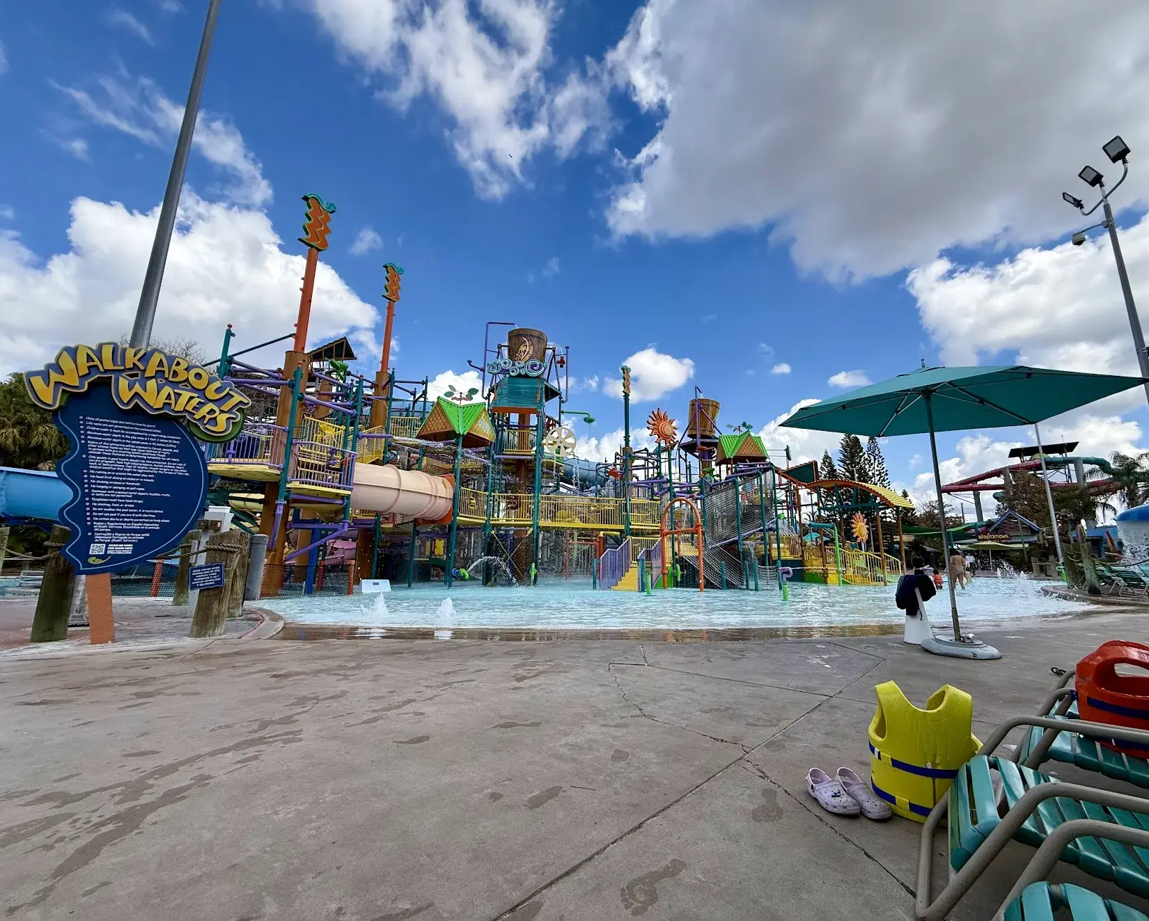 Walkabout Waters, a colorful water play structure at Aquatica Orlando, with a child's life vest and sandals by a lounge chair