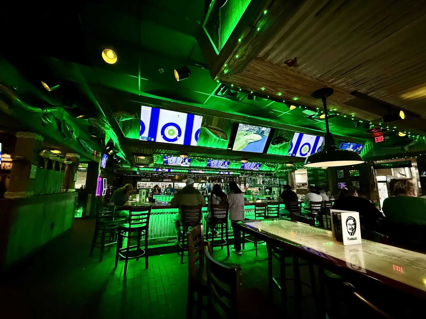 The green-lit bar at Flanigan's, with sports on TV screens and nautical decor