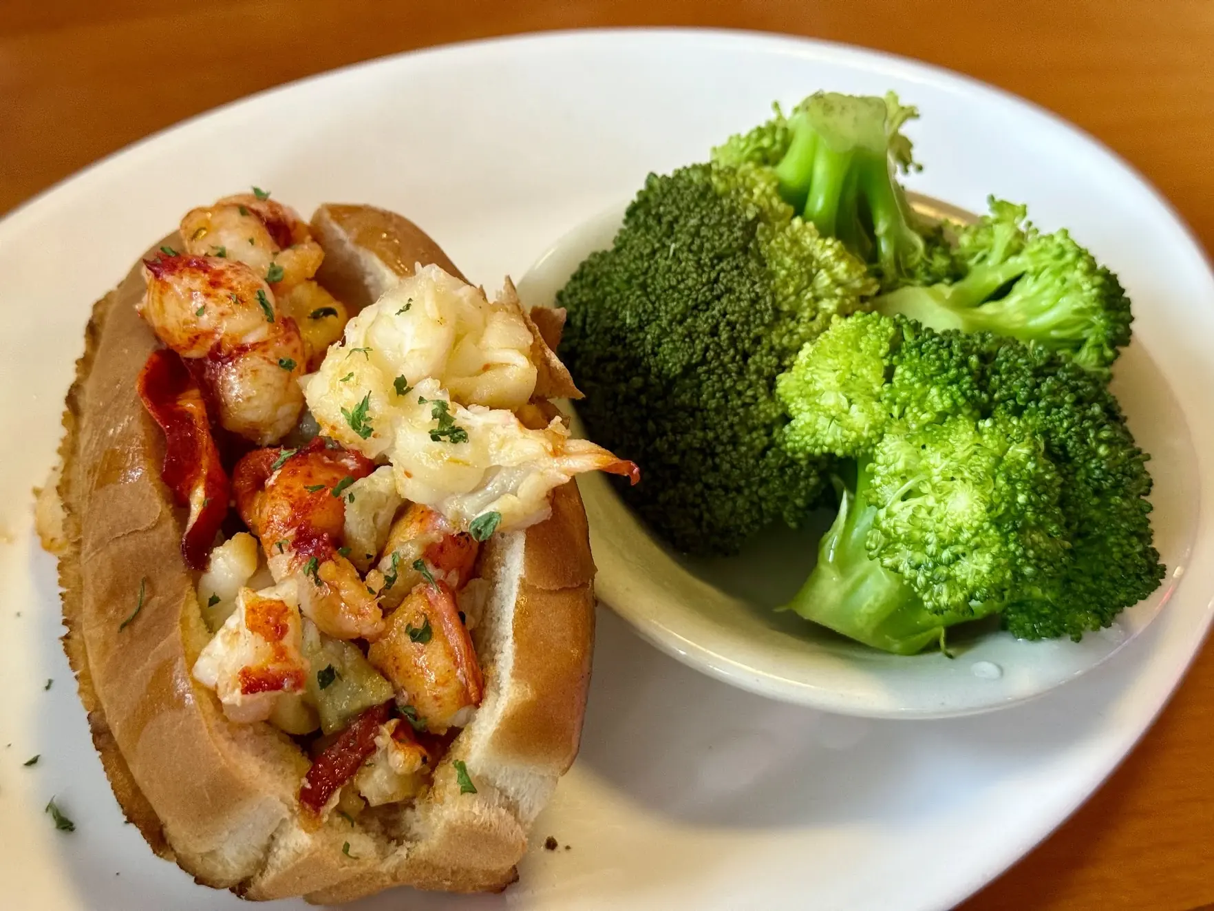 A lobster roll on a toasted bun with a side of steamed broccoli