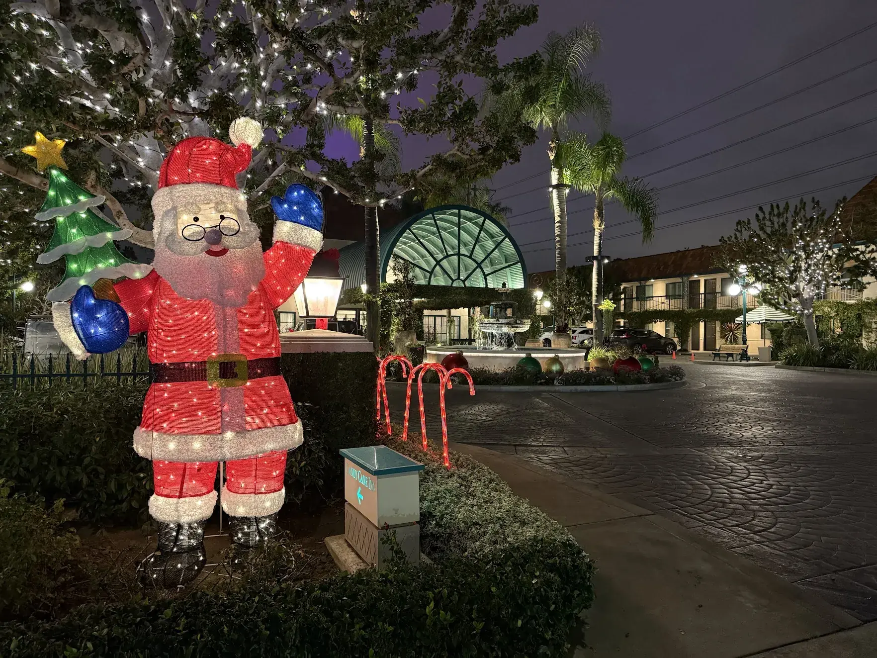 A lit-up Santa Claus figure and candy canes at the Candy Cane Inn driveway, with a fountain behind
