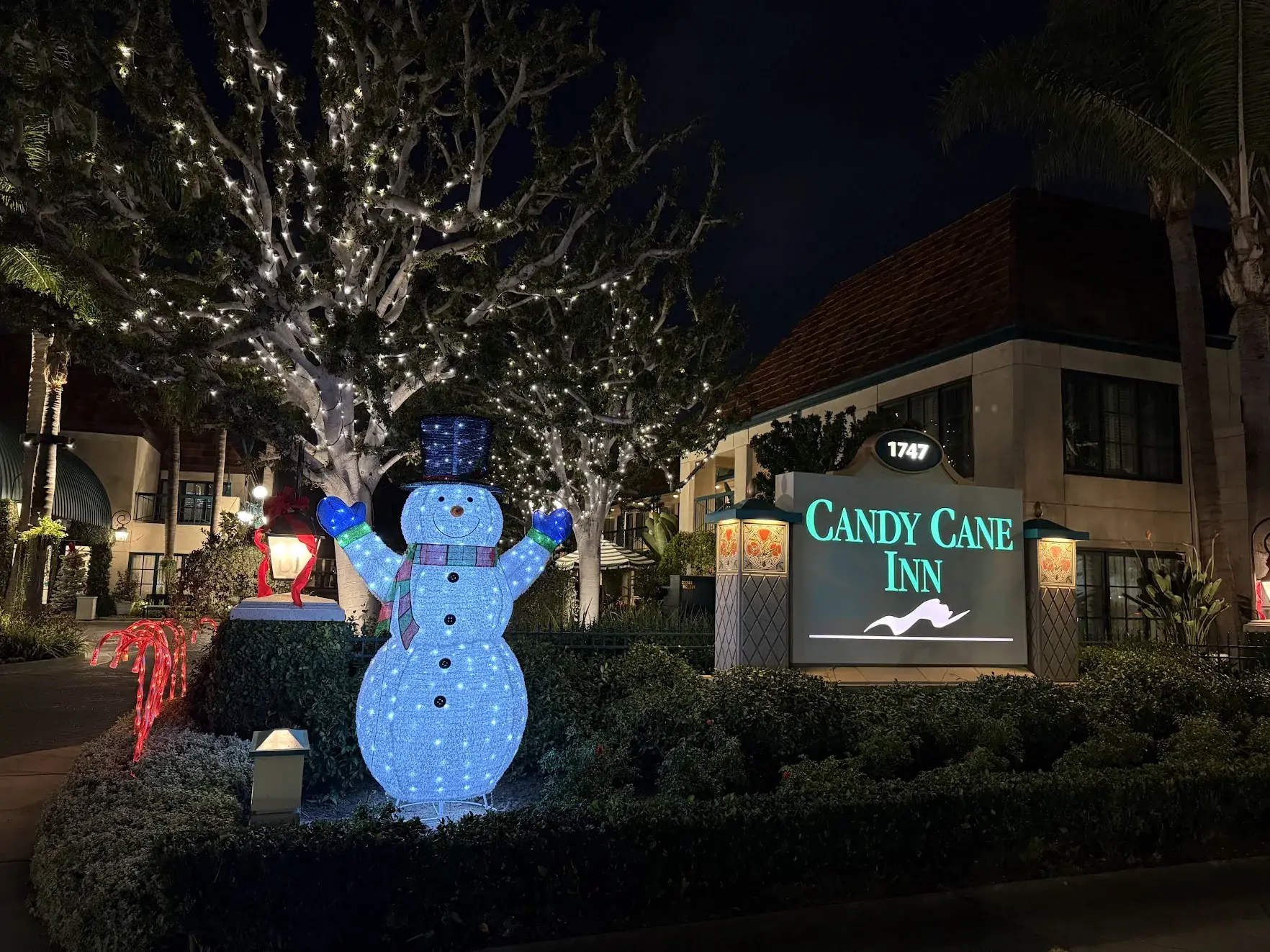 A glowing snowman next to the Candy Cane Inn sign, with Christmas lights in the trees