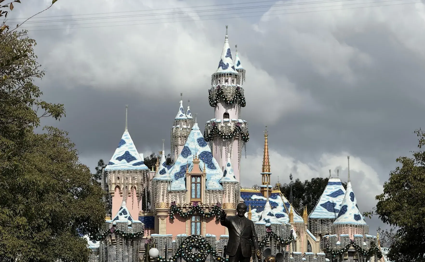 Sleeping Beauty Castle with snow-capped towers and garlands by day, with the Partners statue in front