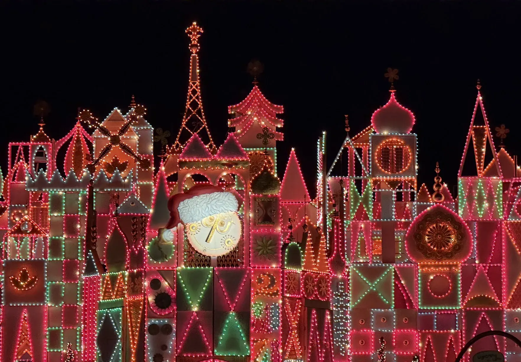 The it's a small world facade covered in red, green and white Christmas lights at night