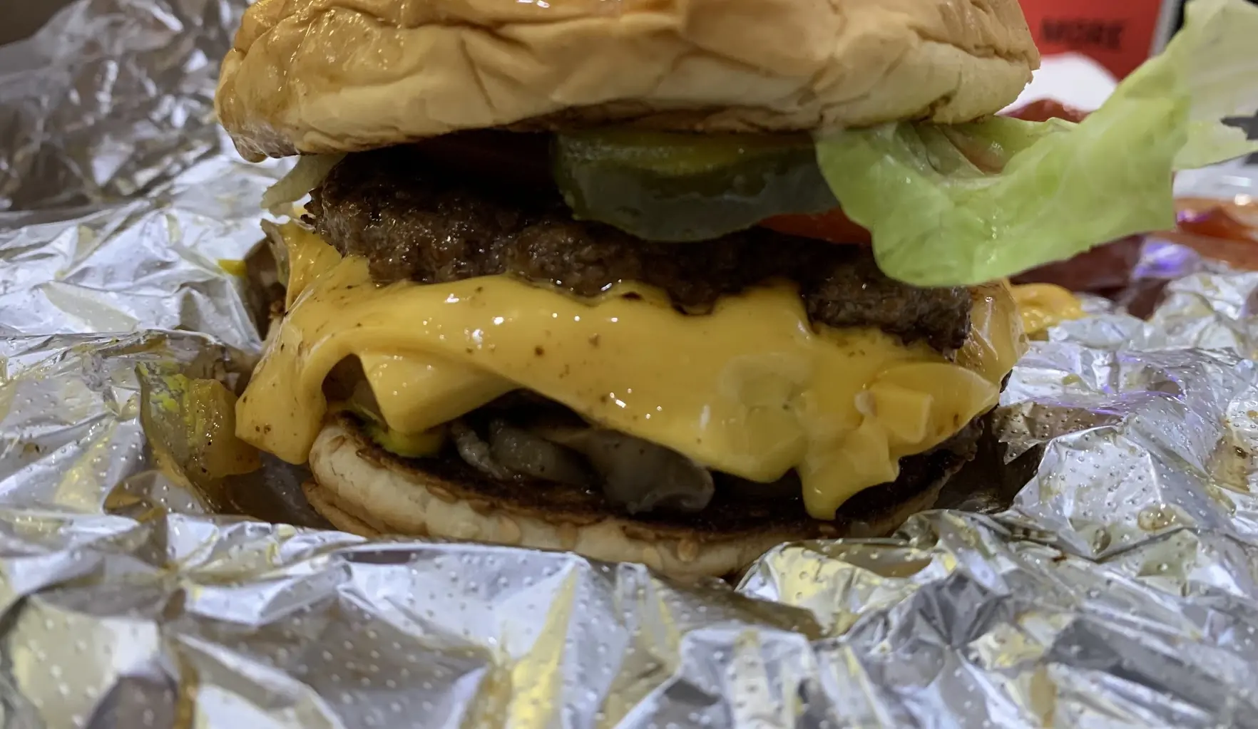 A Five Guys cheeseburger with lettuce, tomato and pickles on its foil wrapper