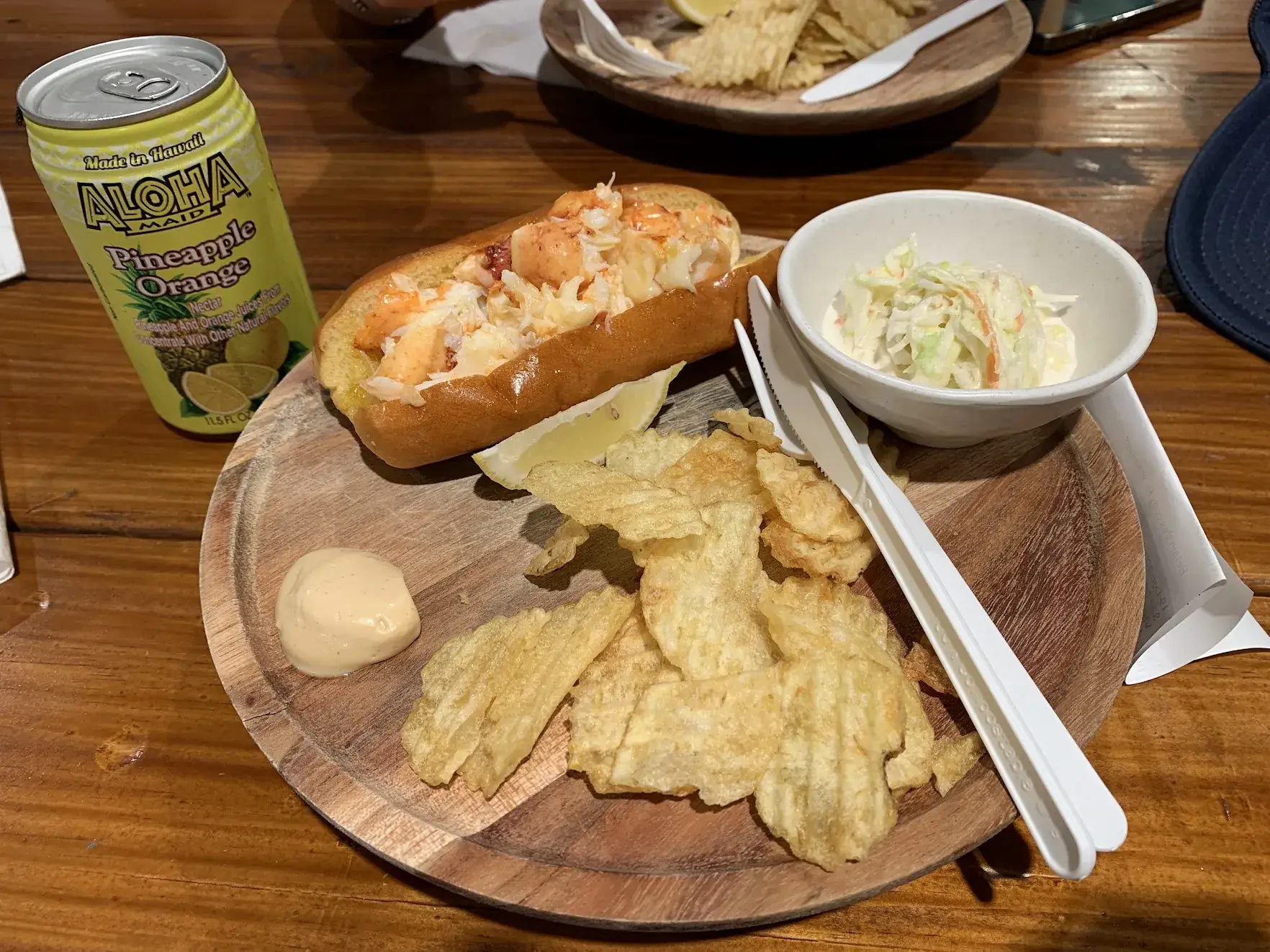 A lobster roll with potato chips, coleslaw and a can of Aloha Maid pineapple-orange juice