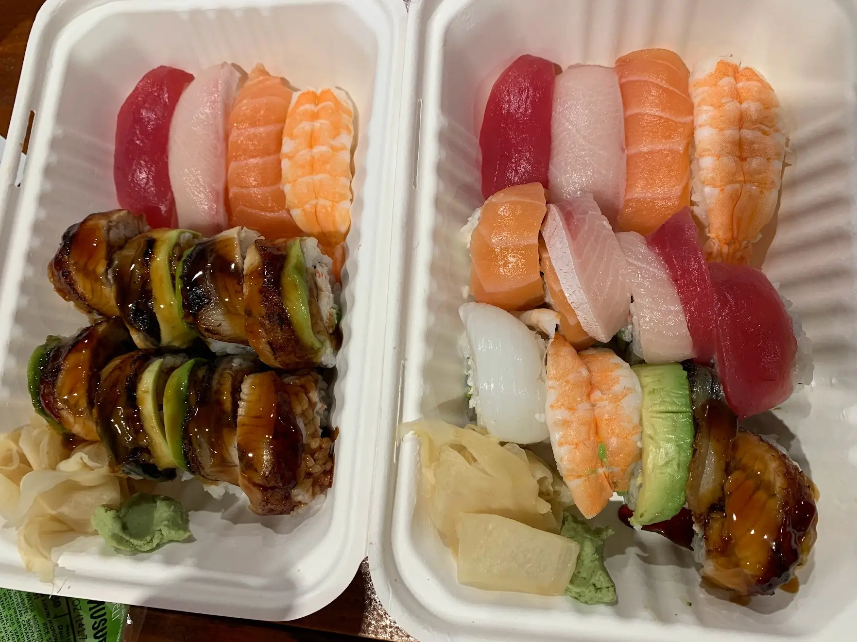Two takeout boxes of nigiri sushi and eel rolls with ginger and wasabi