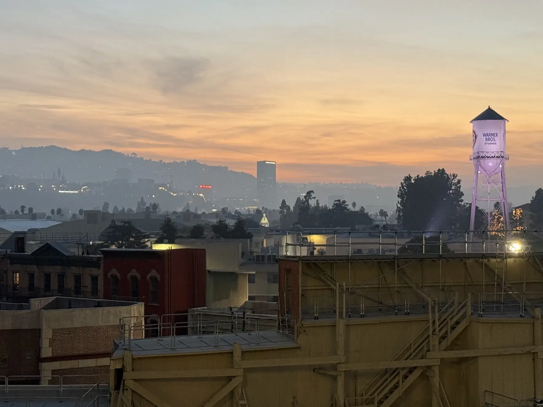 The Warner Bros. water tower lit up at sunset above the backlot rooftops, with the Hollywood Hills behind